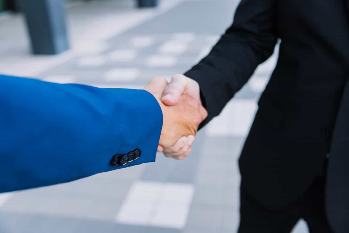 Duas pessoas apertando as mãos em acordo de negócios na rua, símbolo de parceria e sucesso profissional.